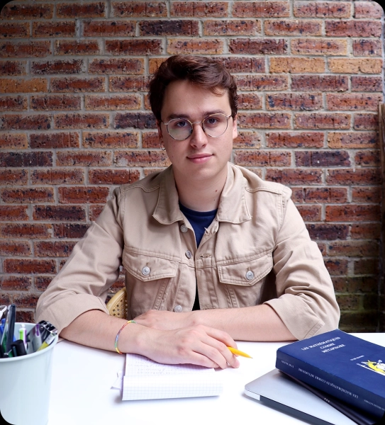 Мужчина сидит за белым столом с карандашом и бумагой для заметок в руках.