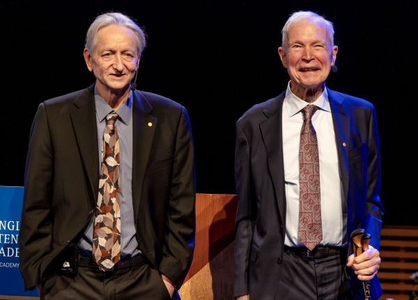 Двое улыбающихся мужчин в костюмах стоят рядом.