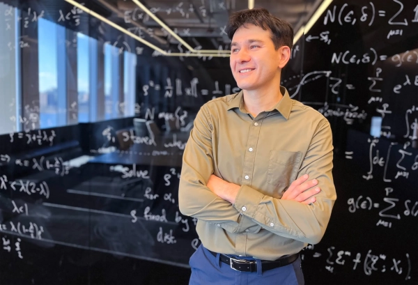 Улыбающийся мужчина со скрещенными руками стоит перед доской.