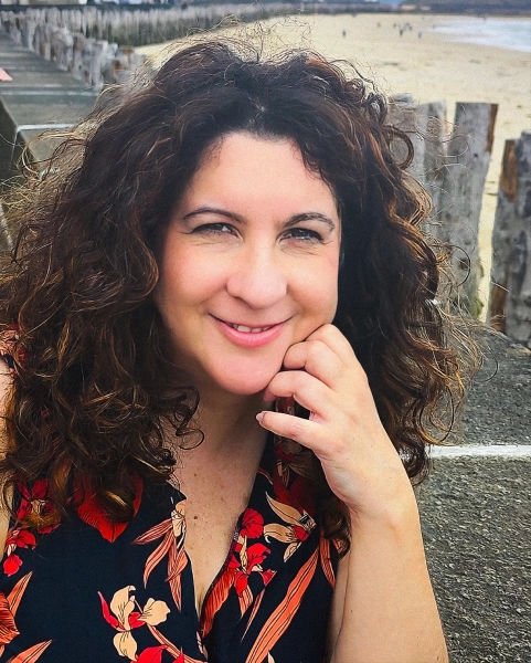 Женщина с вьющимися волосами позирует на пляже.