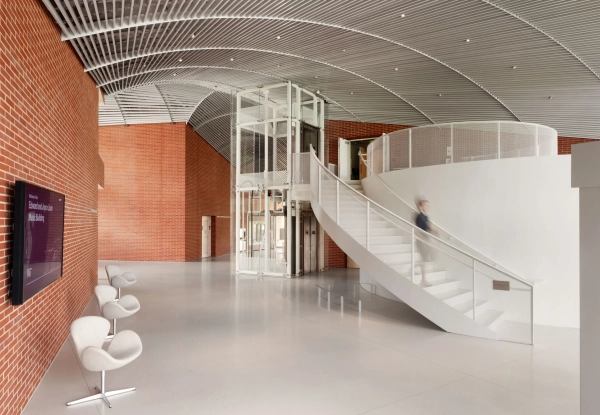 вестибюль с кирпичными стенами и отдельно стоящим лифтом рядом с белой лестницей