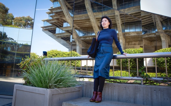 Роуз Ю в темном свитере и юбке прислонилась к ограждению перед рядом зеркал.