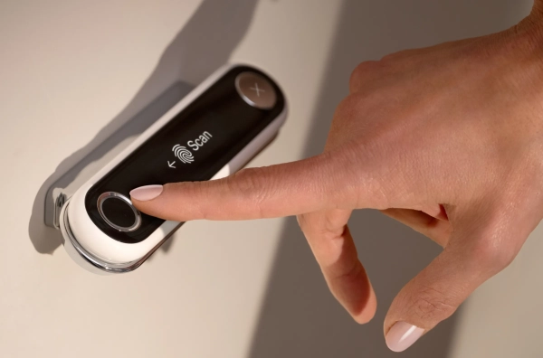 Человек прикладывает палец к настенному сканеру отпечатков пальцев.