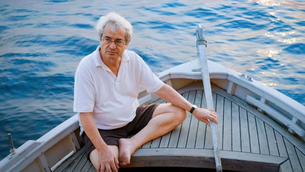 Мужчина управляет небольшой деревянной парусной лодкой.