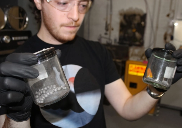 Питер Годарт держит две стеклянные банки: одну с металлическими сферами, а другую с плоскими металлическими фигурами.