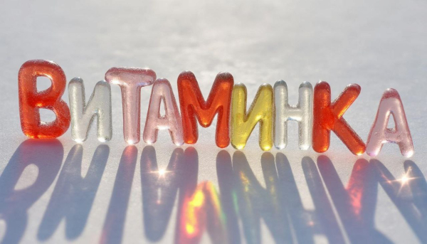 Prompt: На солнечном свету сверкают яркие прозрачные леденцы в виде букв, которые складываются в слово Витаминка. Свет проходит сквозь леденцовые буквы, как сквозь витражи, и оставляет разноцветные отражения на белой глянцевой поверхности. Высокая детализация