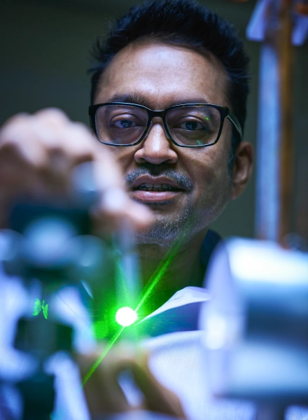 На снимке запечатлен мужчина, работающий с зеленым лазером в темной лаборатории.