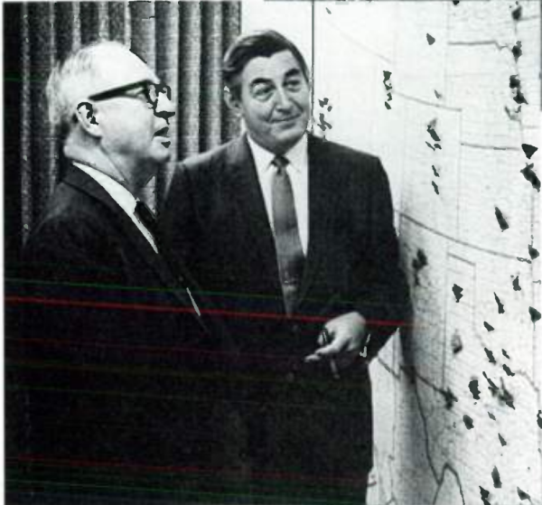 Тэнди (справа) с другим руководителем и его фирменной сигарой перед картой расположения магазинов Radio Shack (Ирвин Фармин, «Денежная машина Тэнди», вставка с фотографией).