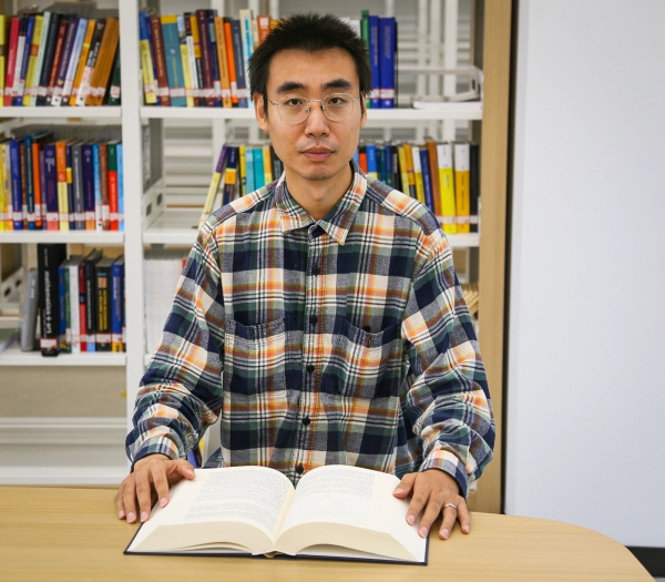 Мужчина сидит за столом, перед ним открытая книга.