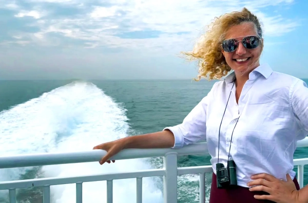 Женщина в солнцезащитных очках стоит на палубе самолета Halunder Jet, ее волосы развеваются на ветру.