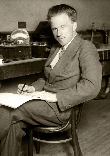 Фотография в стиле сепия, на которой изображен молодой человек с тихой улыбкой, пишущий в блокноте, лежащем у него на коленях.