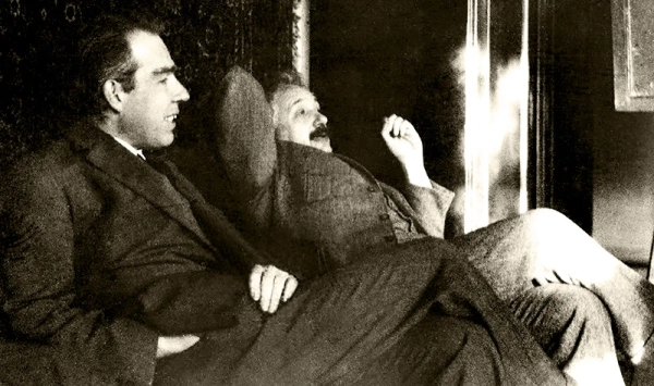 : Черно-белая фотография двух мужчин в костюмах, сидящих рядом, откинувшись назад, и беседующих о чем-то.