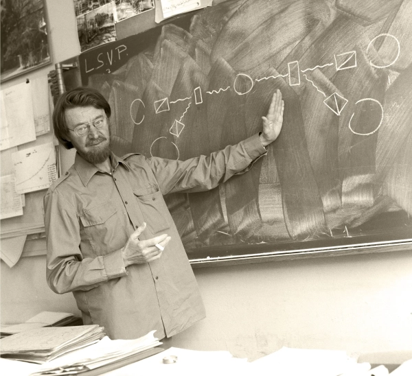 Бородатый мужчина указывает на доску.