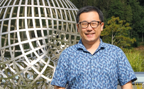 Мужчина в очках стоит перед скульптурой.