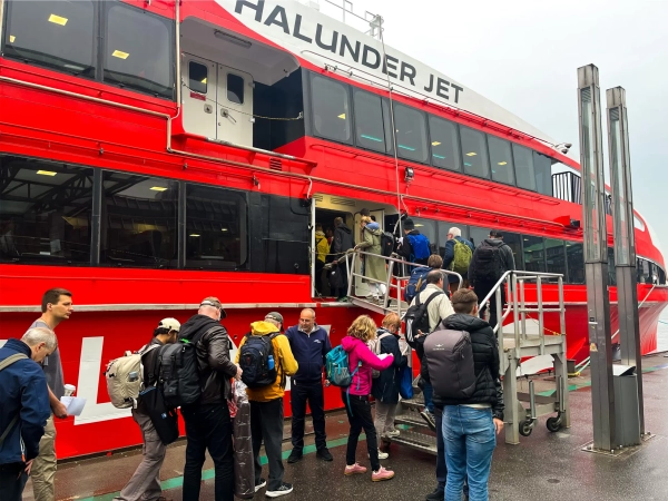 Физики выстраиваются в очередь, чтобы подняться на борт большого красно-белого катера Halunder Jet.