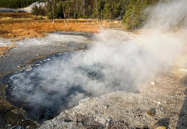 Из серого горячего источника поднимаются клубы пара.