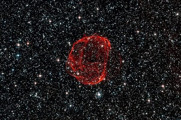 Красный остаток сверхновой в космосе на фоне звёзд.