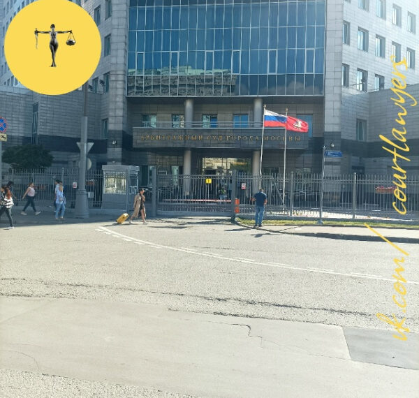 Здание арбитражного суда Москвы с флагами, прохожие на тротуаре в солнечный день.