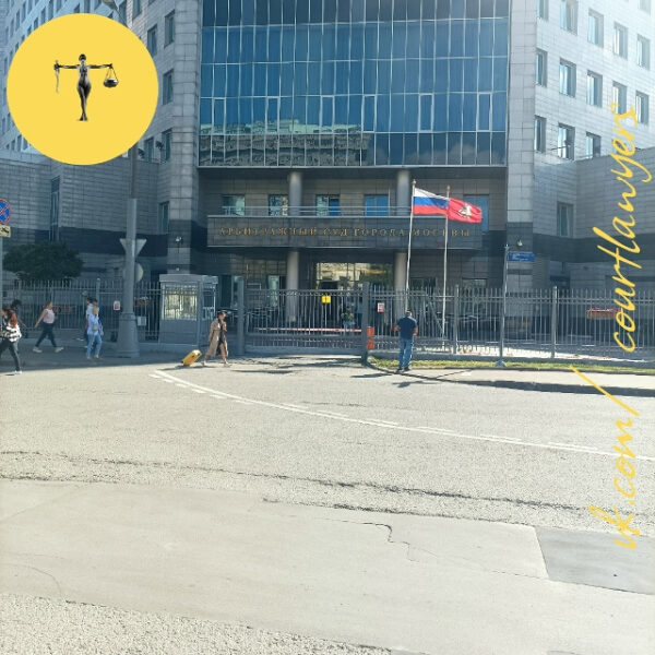 Здание арбитражного суда Москвы с флагами, прохожие на тротуаре в солнечный день.