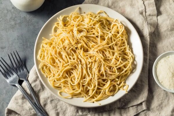 Спагетти с сыром и перцем на белой тарелке, рядом вилки и сыр.