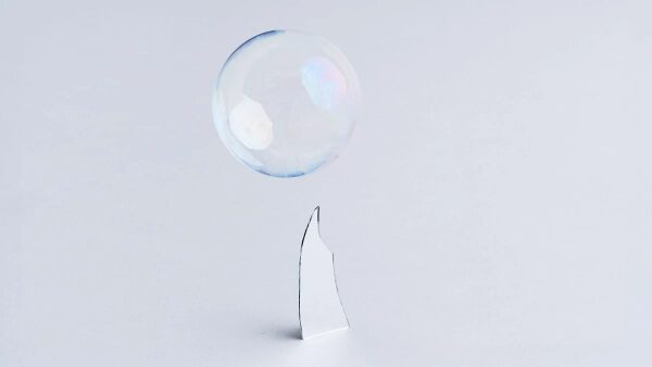 Мыльный пузырь на острие зеркального осколка на светлом фоне.