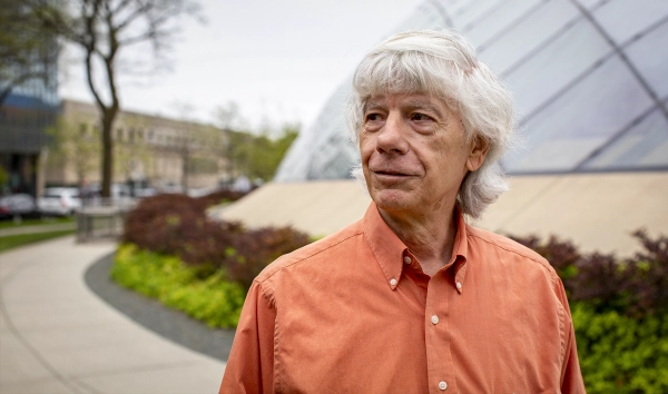 Фотография крупным планом мужчины в ярко-оранжевой рубашке, стоящего снаружи.