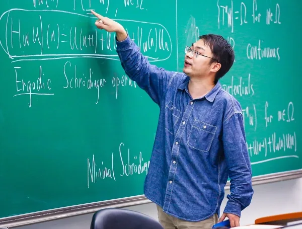 Доказательство «Десяти мартини» использует теорию чисел для объяснения квантовых фракталов. 10 Мужчина в темно-синей рубашке стоит перед книжным шкафом.