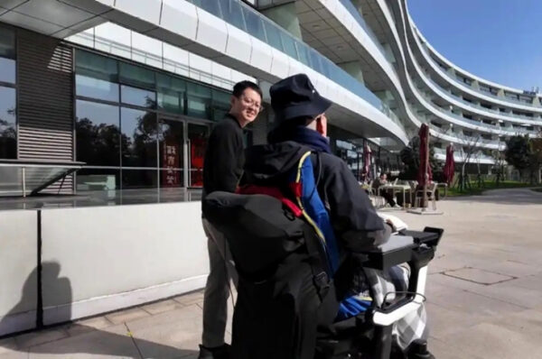 Человек в инвалидной коляске перед современным зданием под открытым небом.