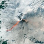 Спутниковый снимок извержения вулкана: поток раскалённой лавы на заснеженном склоне.