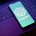Смартфон с логотипом ChatGPT на клавиатуре ноутбука в фиолетовом свете.