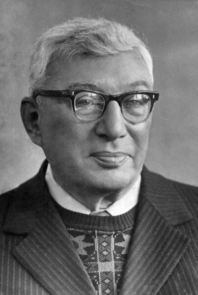 Пожилой человек в костюме и очках на черно-белом портрете.