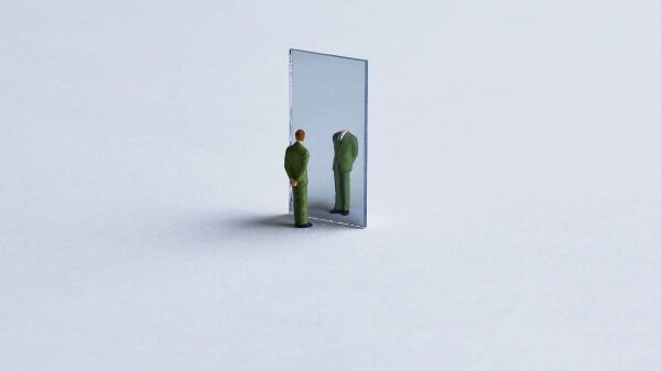 Миниатюрная фигурка перед зеркалом, отражающим только одежду без головы.