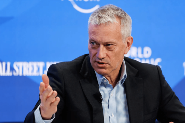 Мужчина в костюме выступает на форуме с синим баннером на заднем плане.