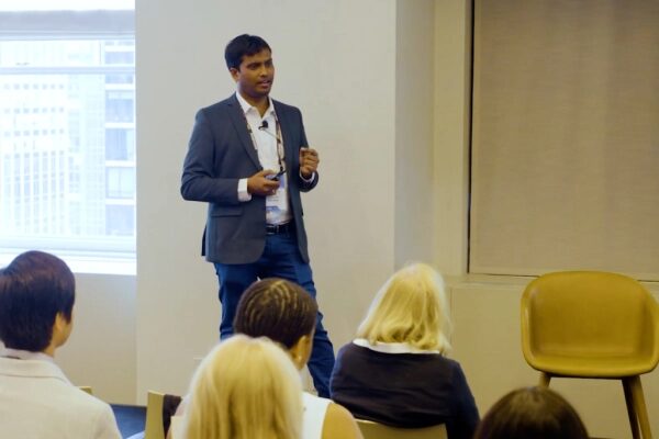 Мужчина в костюме выступает перед аудиторией в офисной обстановке.