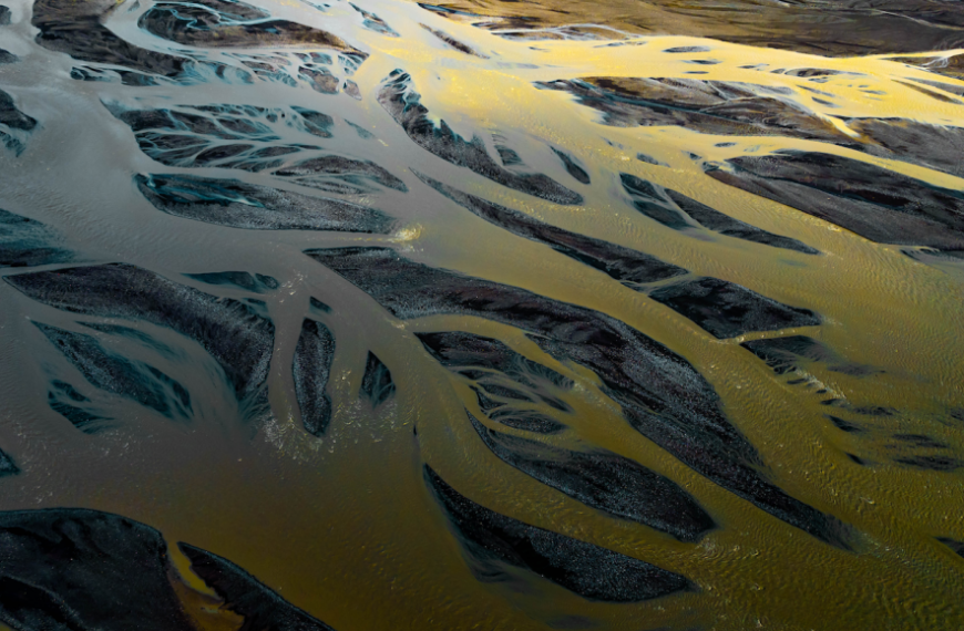 Аэрофото извилистой реки с разноцветной водой и песчаными отмелями.