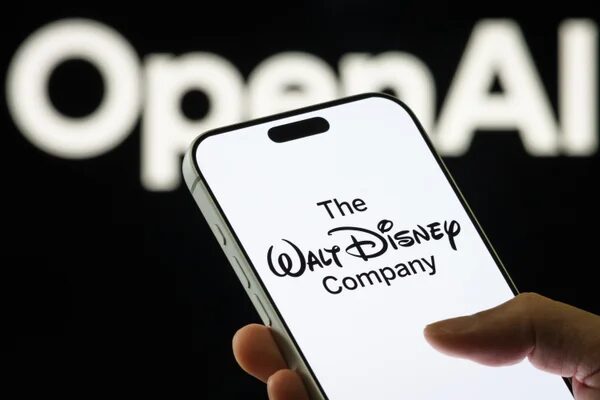 Смартфон с логотипом Disney на фоне текста OpenAI, в руке человека.
