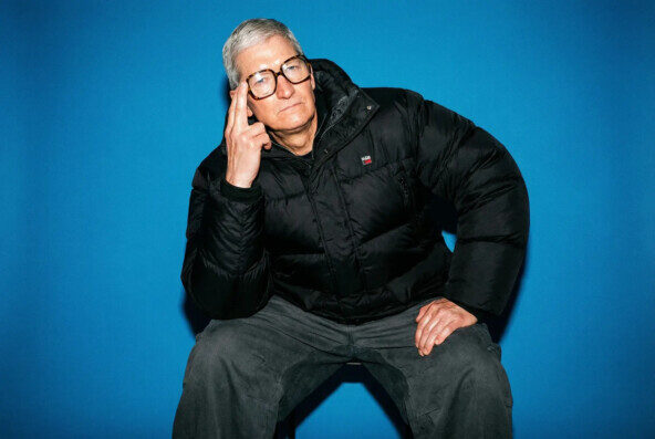 Мужчина в очках и черной куртке позирует на синем фоне.