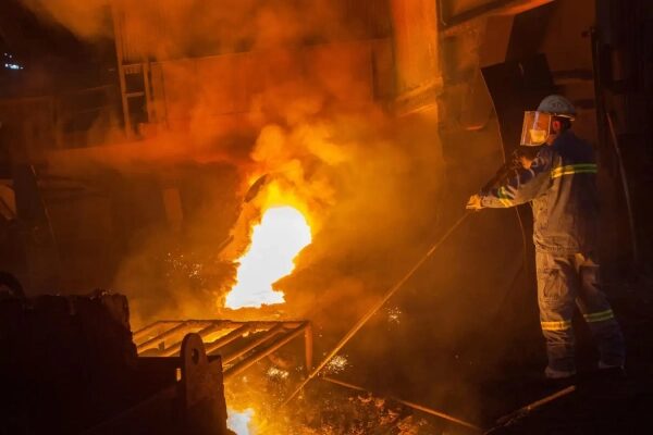 Рабочий в защитной экипировке у плавильной печи на металлургическом заводе.