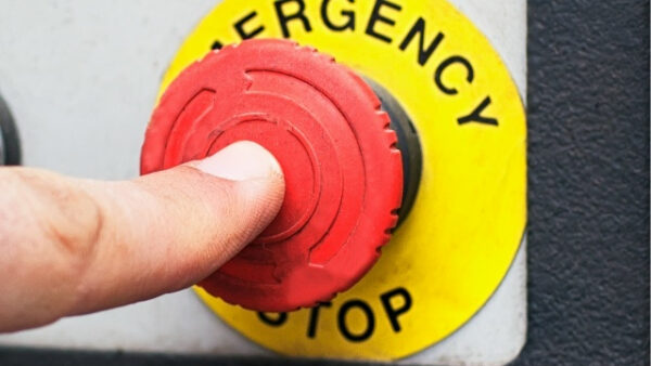 Палец нажимает красную кнопку аварийной остановки на пульте управления.