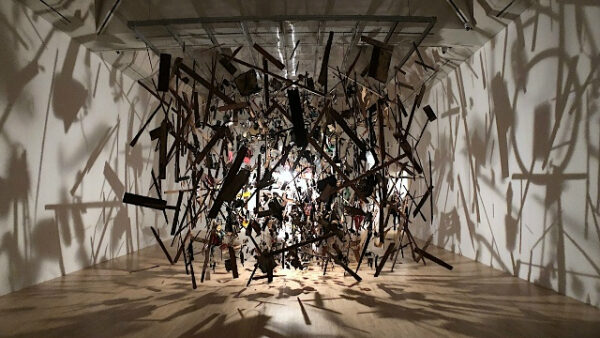 Инсталляция из подвешенных деревянных объектов, создающих тени на стенах галереи.