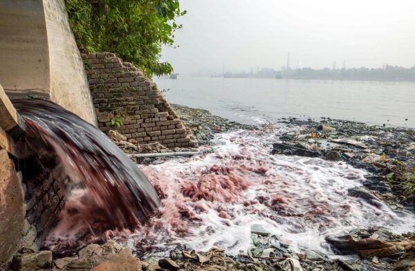 Цветная вода вытекает из цементного туннеля в реку, а на заднем плане виднеется город.