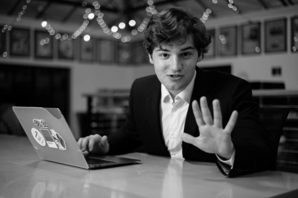 Молодой человек в костюме у ноутбука, сидит за столом, жестом показывает остановку.
