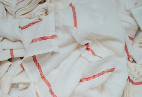 Куча белых полотенец с красными полосками, лежащих на фоне.