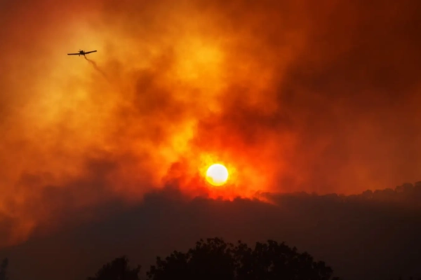 Самолет 2GME5J3 оставляет за собой след из химикатов, используемых для борьбы с лесным пожаром. Эффектный красный дым на фоне заходящего солнца.