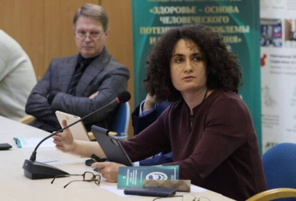 Женщина и мужчина обсуждают на конференции тему здоровья, сидя за столом с микрофонами.