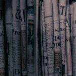 Старые газеты, уложенные в ряд на полке для чтения или коллекционирования.