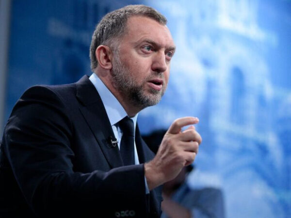 Мужчина в костюме жестом объясняет что-то на фоне синего здания.