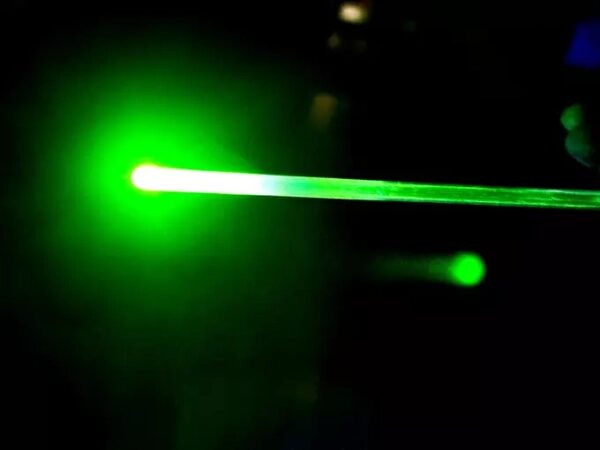 Зеленый лазерный луч в темноте, освещающий пространство.