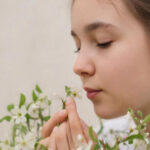 Женщина держит цветущие ветви с белыми цветами на фоне светлой стены.