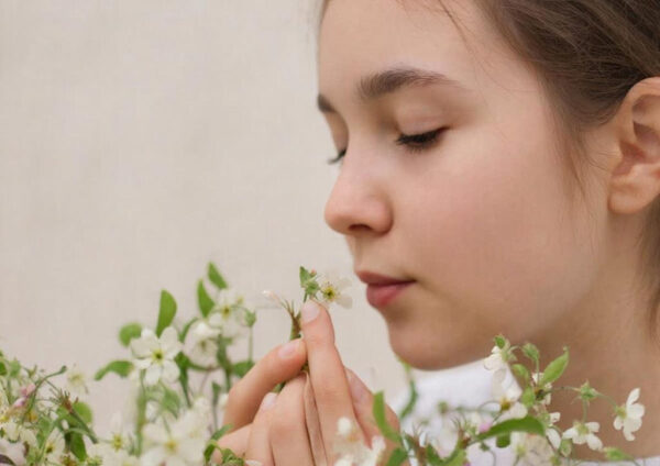 Женщина держит цветущие ветви с белыми цветами на фоне светлой стены.